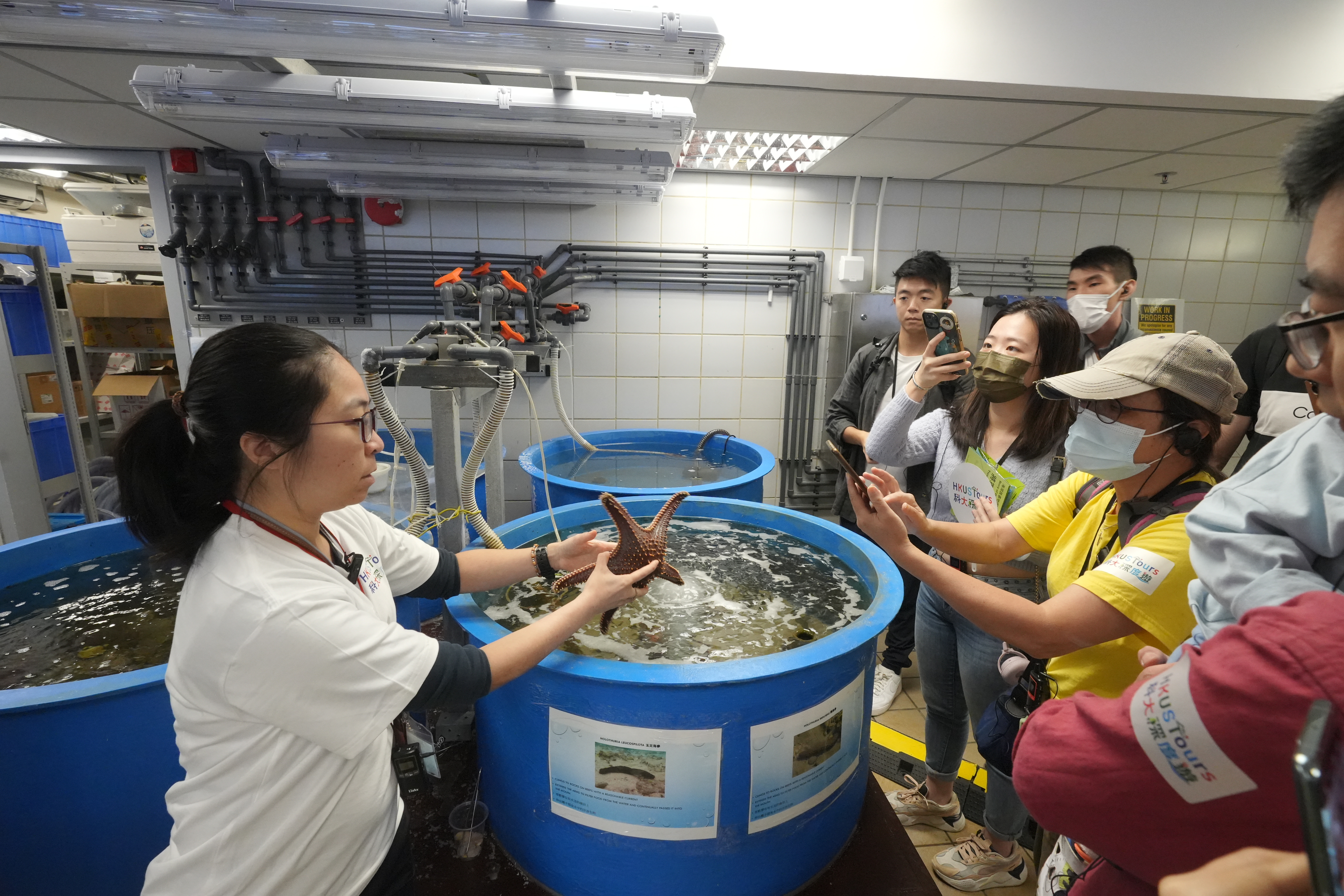热爱海洋的Bernadette（左一）为参加者介绍科大海滨，和周边的海洋生物教学和研究设施。在实验中心，Bernadette亦特意展示海星、马蹄蟹等各种海洋生物，讲解香港海洋生态的历史和现况，并让参加者近距离观赏和接触。  Bernadette说看到大家非常兴奋，也踊跃发问及留影，令她感到由衷的满足。