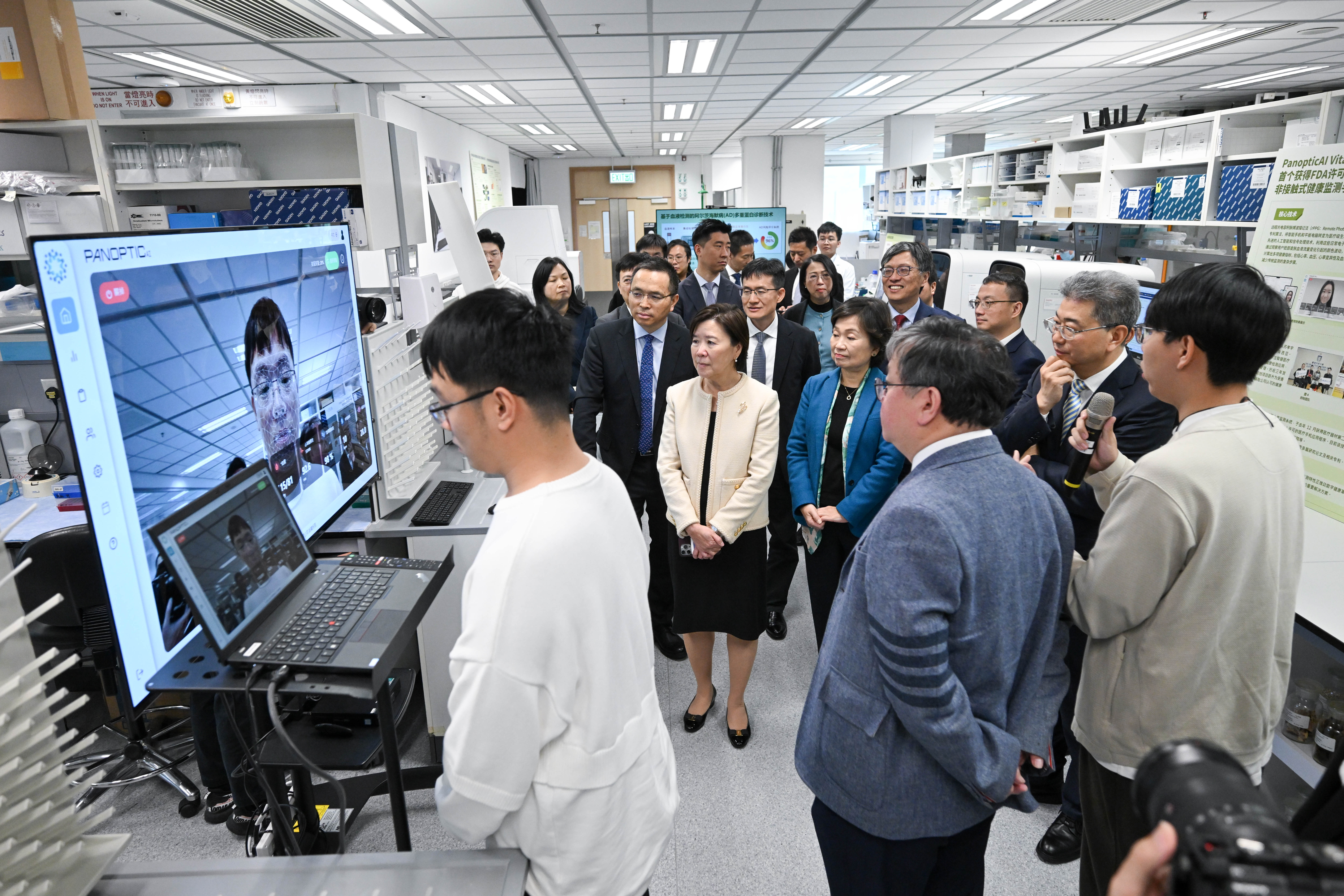 工學院副院長蘇孝宇教授團隊的兩位學生周松堂（右一）、侯俊杰（左一）介紹全球首個獲美國食品藥物管理局許可的非接觸式健康檢測手機應用程式。 