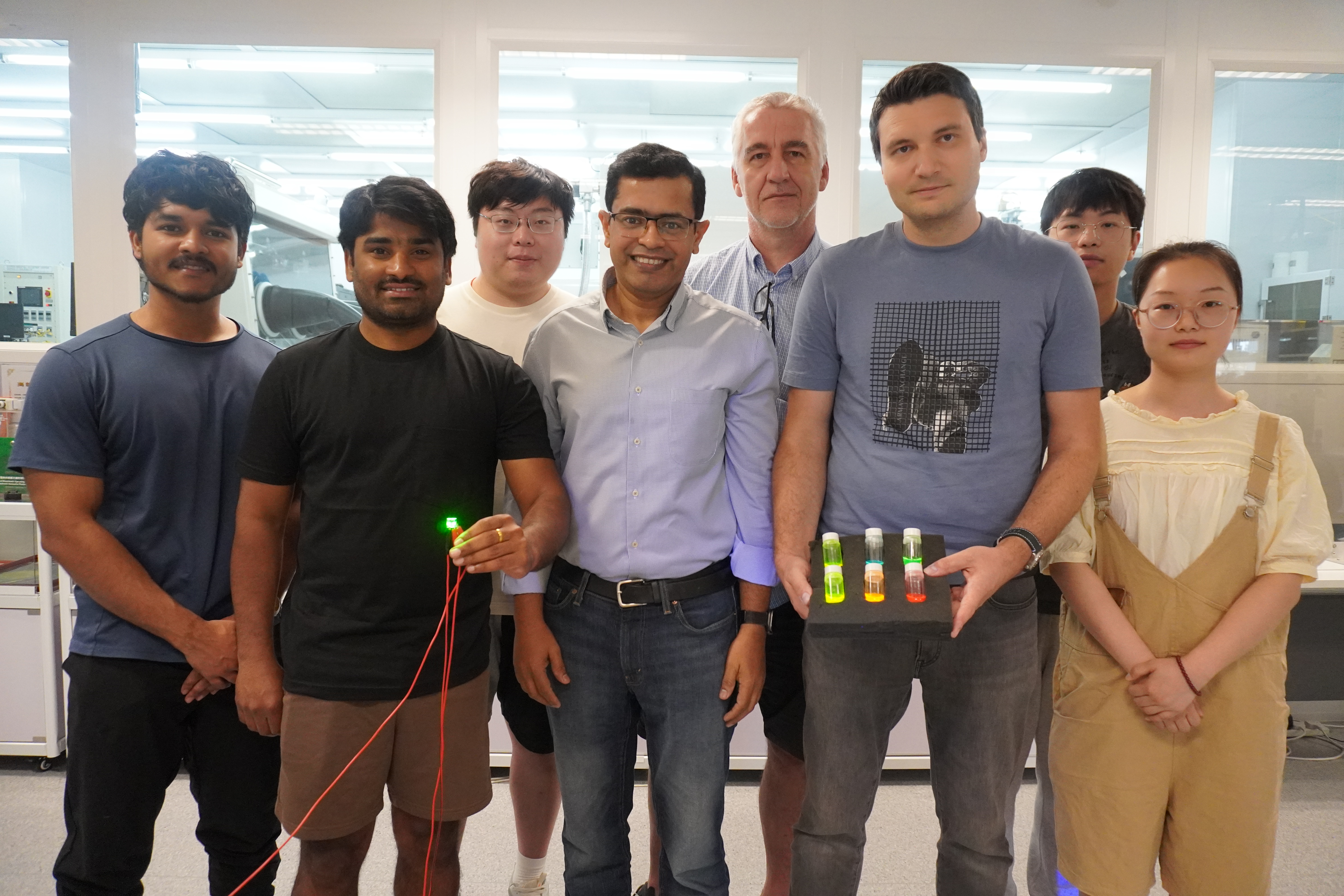 A group photo of Prof. Abhishek K. SRIVASTAVA (first row, center), Dr. Maksym PRODANOV (first row, second right) and PhD candidate Mr. Kumar MALLEM (first row, second left) with members of their research team. In the photo, Dr. Prodanov holds three bottles with quantum rod materials while Mr. Mallem holds a green emitting QRLED sample.