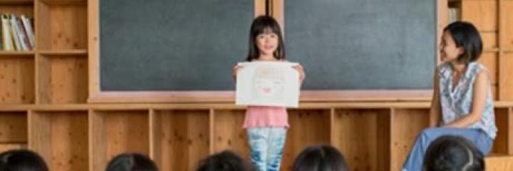 Young girl presenting in class with the teacher on the side